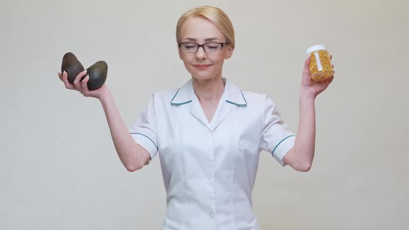 Nutritionist Doctor Holding Organic Avocado Fruit and Jar of Medicine or Vitamin or Omega 3 Capsules alt