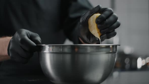 Chef in Black Gloves Squeezes Lemon To the Metal Bowl in Slow Motion, Lemon Sprinkles, Raw Natural alt