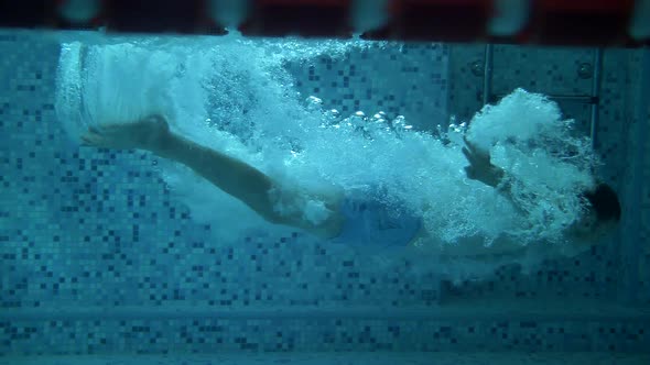 Athlete swimmer dives underwater in a pool with blue water. Super slow motion alt