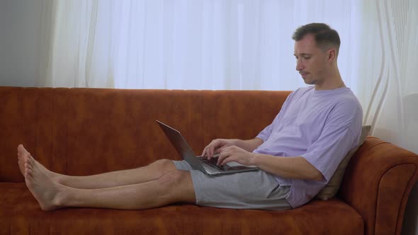 A Man Works at a Laptop From Home Sitting on the Couch