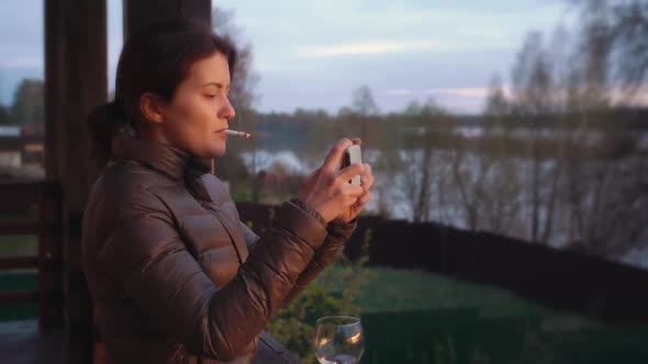 A Young Woman Smokes a Cigarette and Takes Sunset Photos on Her Phone