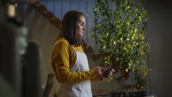Profile of caucasian female jeweller in workshop wearing apron, using tablet, smiling alt
