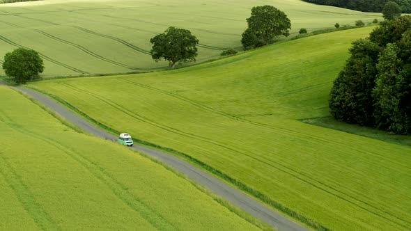 Mini Bus Driving On Narrow Country Road, With Green Fields On Both Sides, Drone Stock Footage 4 alt