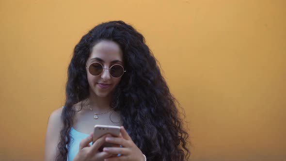 Young Woman with Sunglasses and Smartphone Texting Online in Summer