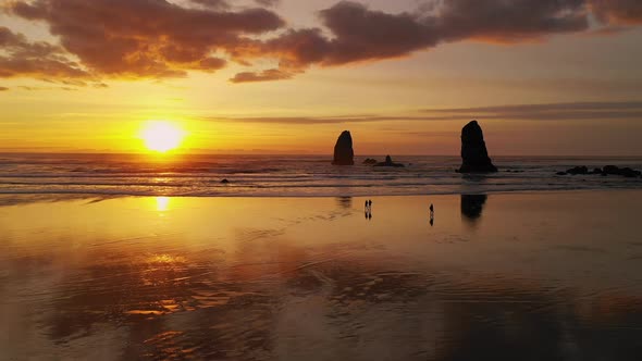 People Walk Cannon Beach as Pacific Ocean Waves Reflect Sunset Glow