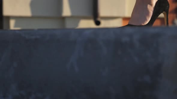 Slim Female Legs in Black Shoes on High Heels Stepping at Sidewalk alt