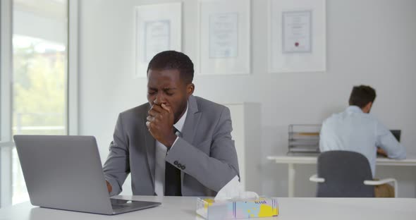Mixedrace Sick Male Manager Cough Sitting at Workplace with Colleague Feeling Worried on Background alt