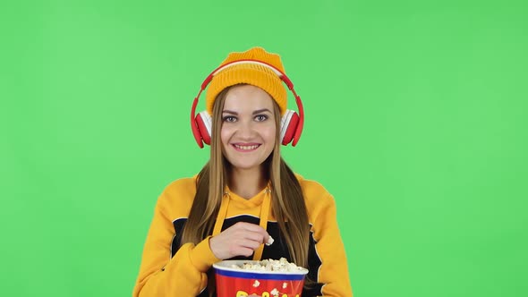 Portrait of Modern Girl in Big Red Headphones Is Watching a Funny Movie and Eating Popcorn. Green alt