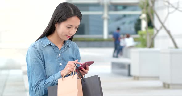 Asian Woman use of mobile phone for shopping with holding shopping bag alt