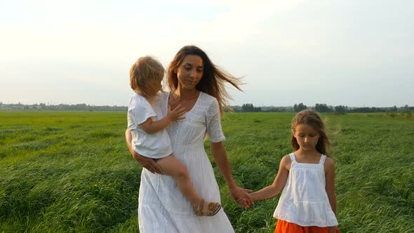 Happy Family, Mother and Her Little Daughters Walk on the Green Grass, Summer Evening