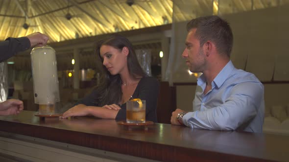 A man and woman couple having a very cold drink at a bar at a tropical island resort alt