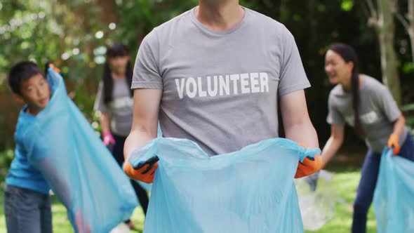 Smiling asian man wearing volunteer t shirt holding refuse sack for collecting plastic waste alt