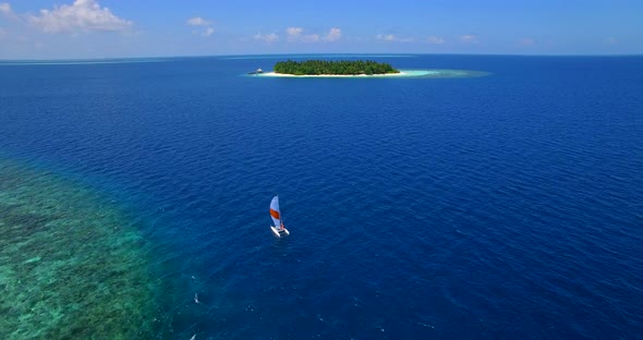 Aerial drone view of a man and woman sailing on a boat to a tropical island alt