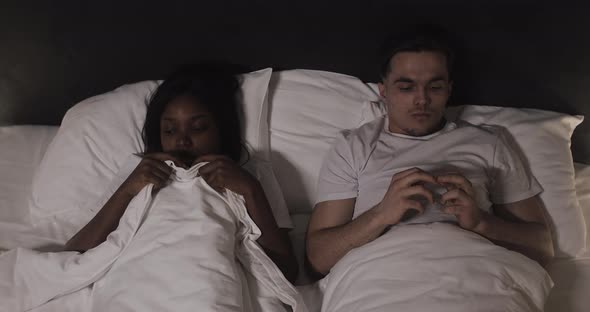 Young Multi-ethnic Couple Lying in Bed at Night. Embarrassed and Shy Young Couple Before First alt