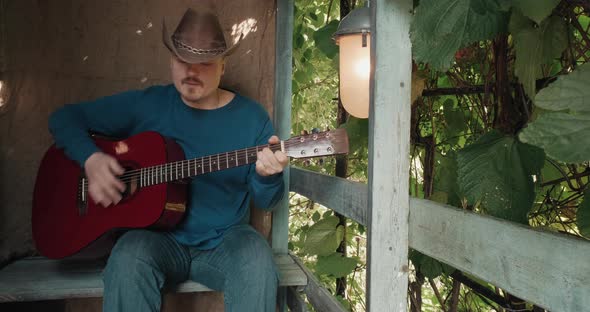 Man with an Acoustic Guitar is Sitting on Porch of House Playing an Instrument