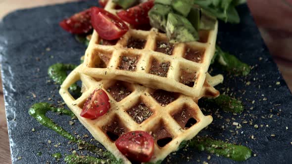 Fresh baked Belgian waffles with arugula, tomatoes and avocado on black a plate. Savory waffles alt