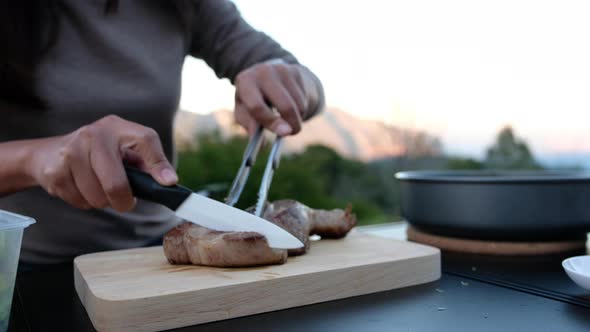 Closeup of a woman cooking and cutting steak with knife while camping outdoors