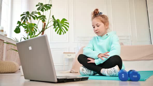 Girl Sitting Near a Laptop with Boredom Looking at the Screen Next to Sports Equipment alt
