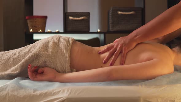 A Young Naked Woman Covered with a Towel Enjoys a Back Massage in a Spa Salon