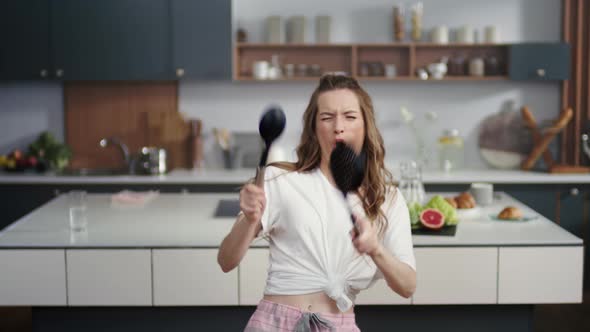 Emotional Woman Playing on Virtual Drums with Spoons on Kitchen Background alt
