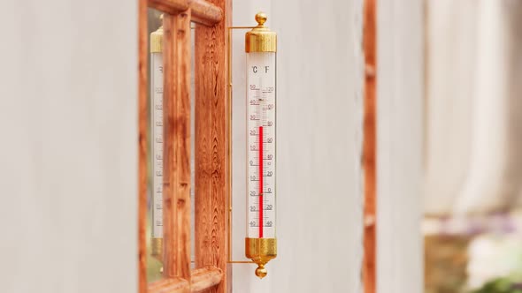 The outdoor thermometer at the garden attached to the wooden window. Warm-season alt