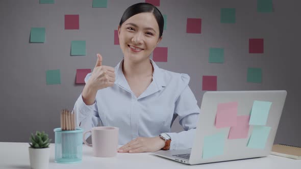 Asian woman happy working looking at camera and showing thumb up.