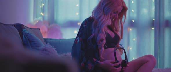 Beautiful pregnant woman putting headphones to her belly for the baby to listen, feeling free, happy alt