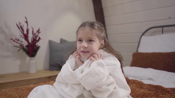 Camera Approaching To Charming Caucasian Girl with Beautiful Eyes Sitting on Bed Dressed in White alt