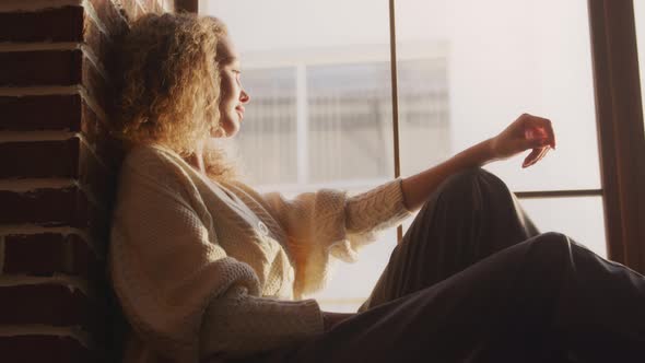 Young Blond Curly Caucasian Woman Sitting on the Loft Window alt