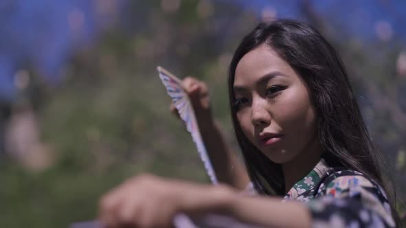 Closeup Portrait of Confident Beautiful Asian Woman Dancing with Fans in Spring Sakura Park Outdoors alt