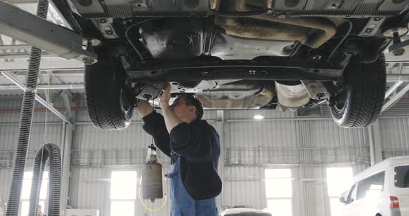 Car Lifted In Automobile Service For Repairing, Worker Fixing Faults Of Brakes alt