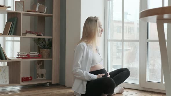 Happy pregnant woman is sitting near large window
