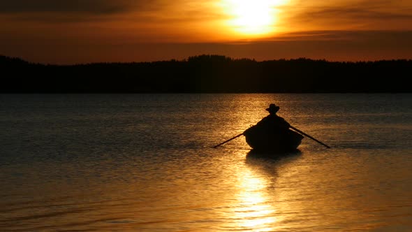 Yellow Sundown Over Lake and Silhouette of Fisherman on Rowing Boat