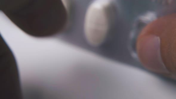 Person Taps with Fingers Pills Blister on Light Surface alt