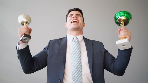 Businessman in Jacket and Tie with Trophy Cups in His Hands Celebrating Victory alt