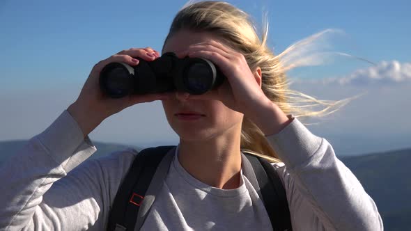 A Young Woman on a Hilltop Looks Around Through Binoculars - Closeup - Mountainous Landscape alt