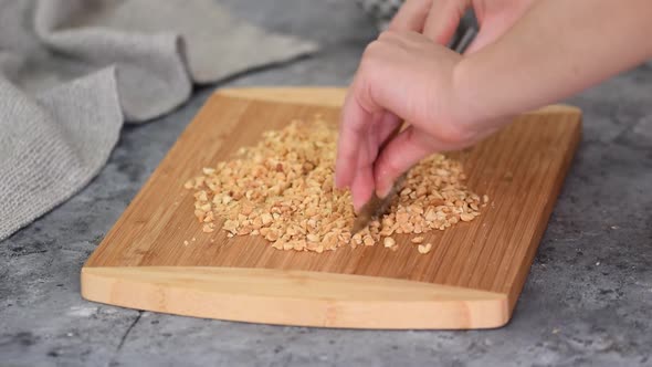 Baker Cuts Nuts with Kitchen Knife on Cutting Board