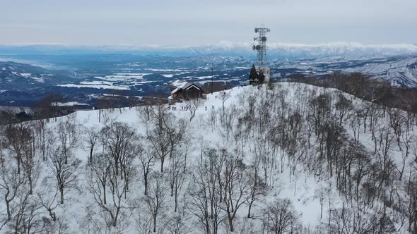 white snow mountain peak in winter at nozawa onsen with skiers and mountain cabin, aerial alt