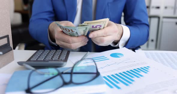 Businessman Counting Money at Table with Documents and Calculator  Movie alt