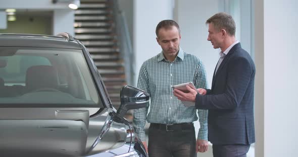 Adult Caucasian Male Trader with Tablet Explaining Specifications To the Customer alt