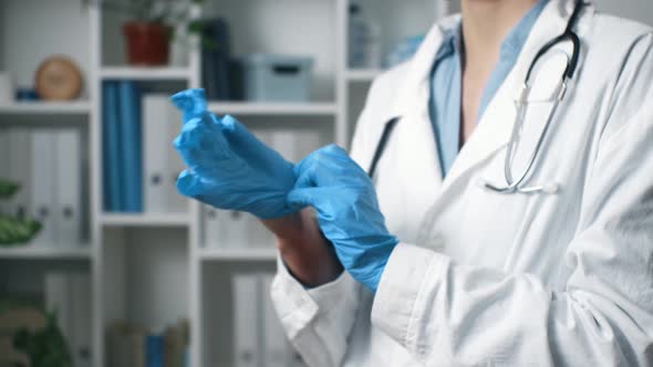 The Doctor Puts On Gloves Close Up. A Medic Stands In A Medical Office Wearing Blue Latex Gloves alt