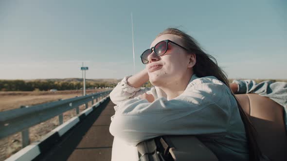 Woman in Sunglasses Rides in Convertible Leaning on Window Looking at Sun