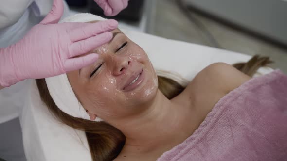 Happy Woman Having Joy During Treatment of Applying Gel on Face By Beautician alt