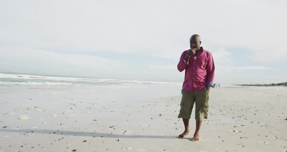 African american senior man walking on a beach rubbing his chin and looking at the sea alt