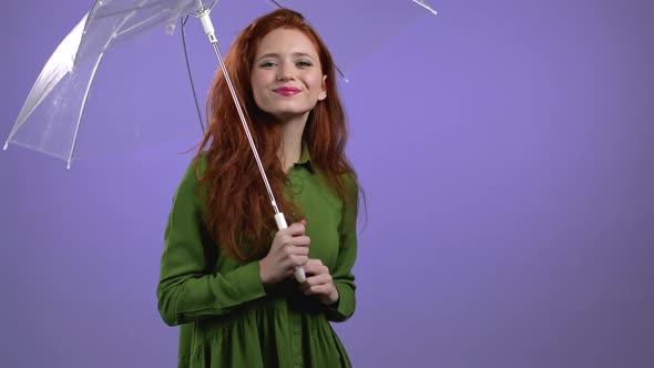 Cute Woman Stands Under Umbrella on Violet Studio Background alt