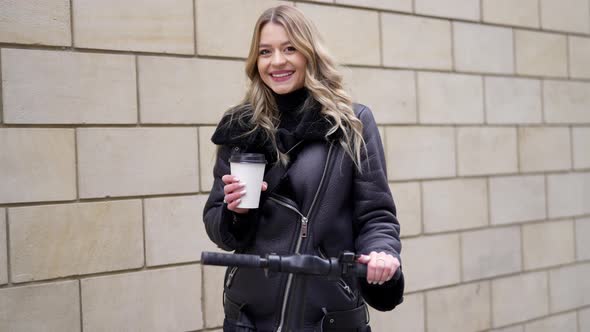 Cheerful Woman with Scooter and Takeaway Coffee alt