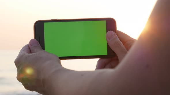 Female holds smart phone with green screen display by sunrise 4K video