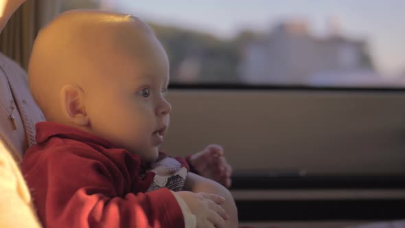 Cute baby girl on mother lap in car looking to the road with curiosity alt