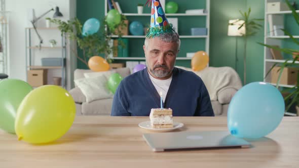 A Depressed Man in a Party Cap Celebrates His Birthday Alone at Home alt