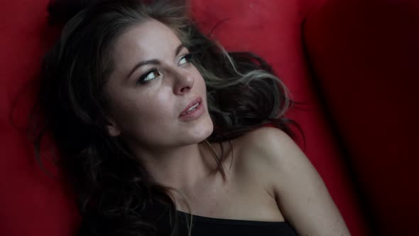 Sexy Playful Woman is Lying on Bed with Red Linen and Flirting with Camera Looking Seductively alt